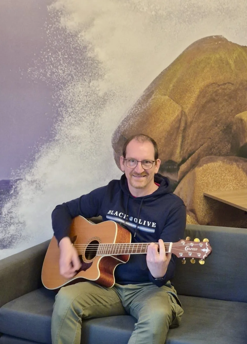 Ich sitze mit meiner Akustikgitarre auf einem Sofa und spiele.